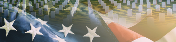 Memorial Day 2024. American flag waving in the foreground with headstones in a VA national cemetery in the background.